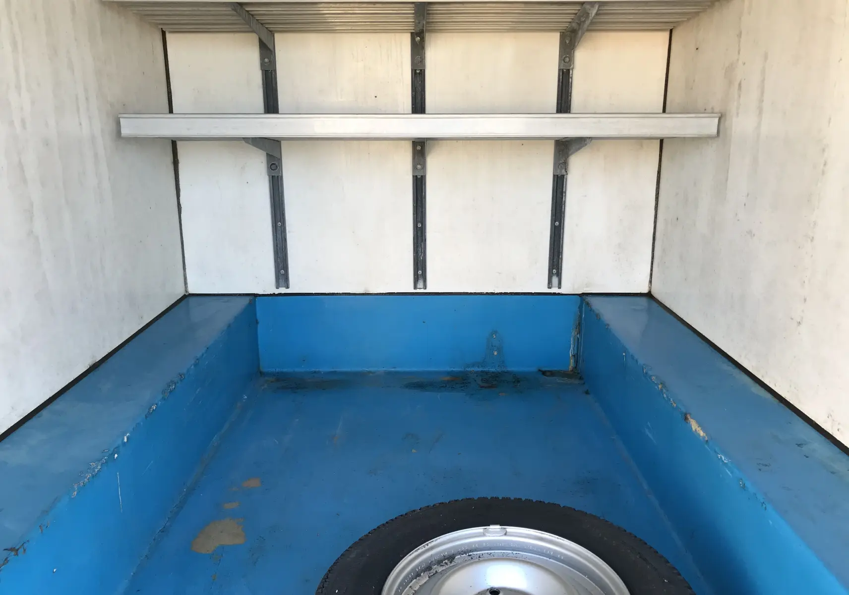 Vue intérieure du coffre isotherme bleu et blanc du Citroën C15 Isotherm blanc de 1997, avec roue de secours visible au sol.