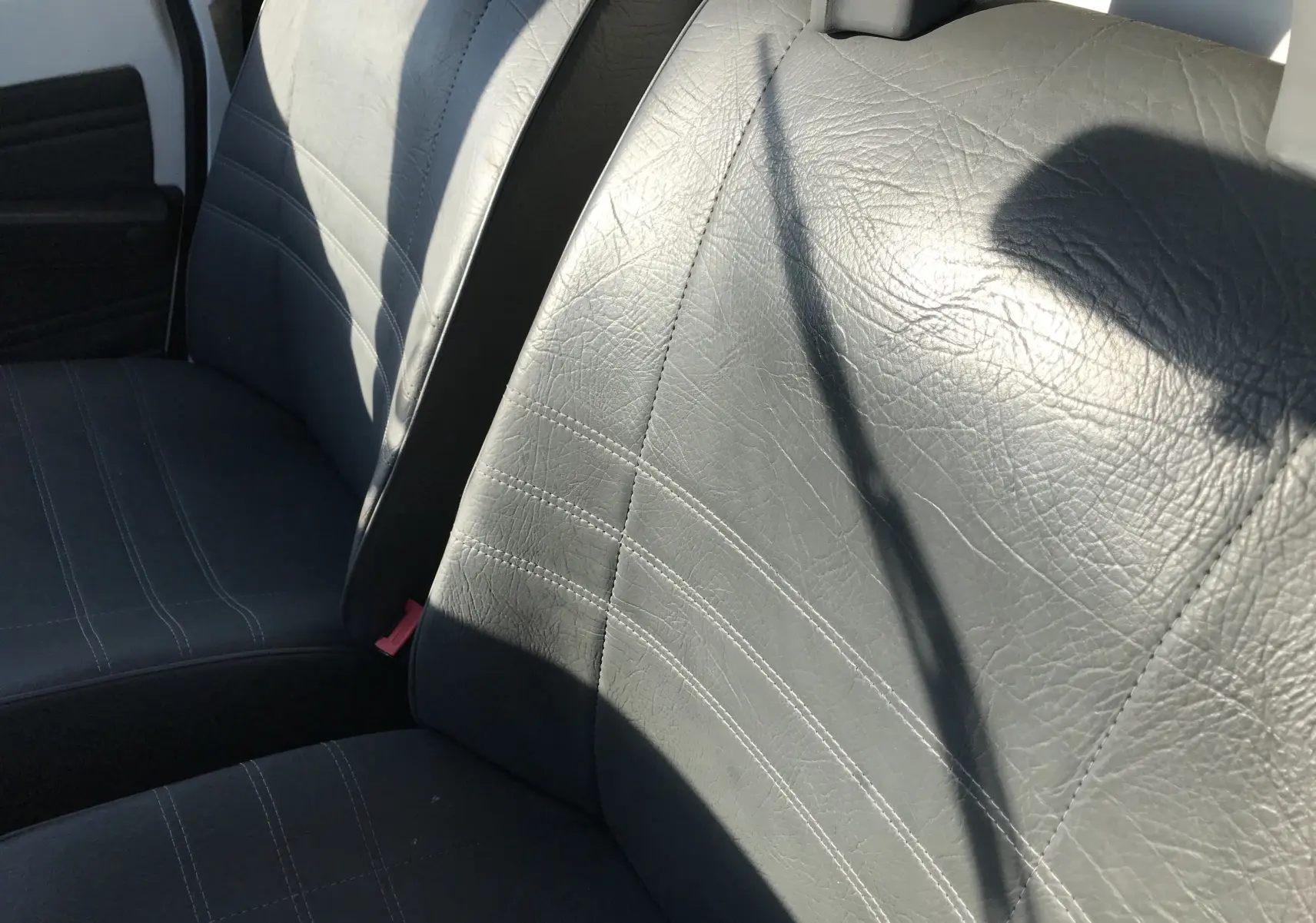 Gros plan sur les sièges avant en cuir noir du Citroën C15 Isotherm blanc de 1997, vue intérieure côté conducteur.