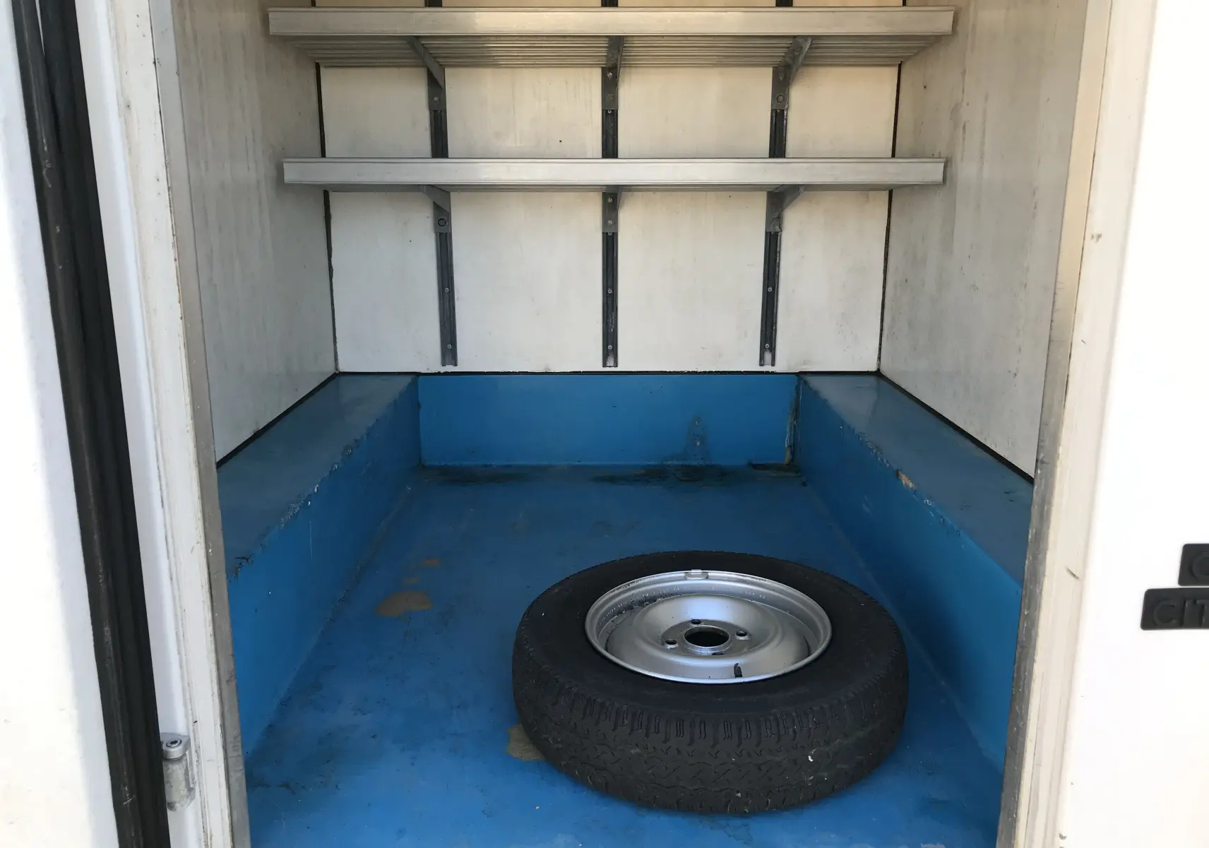 Vue intérieure arrière du fourgon blanc Citroën C15 Isotherm de 1997, montrant un espace de chargement bleu avec une roue de secours.