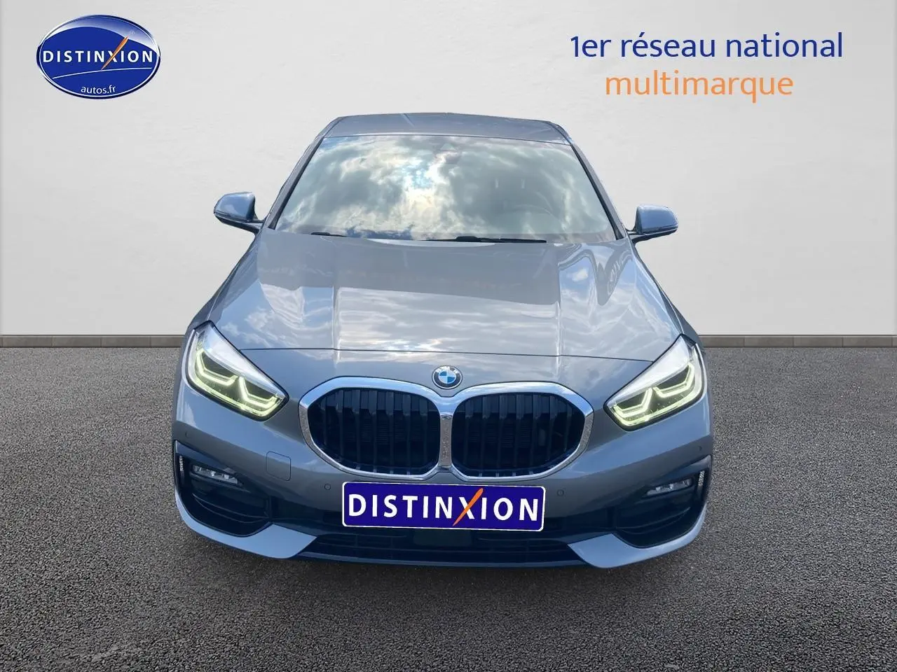 Vue frontale d'une BMW Série 1 gris foncé 2023 avec phares LED allumés et calandre caractéristique double haricot.