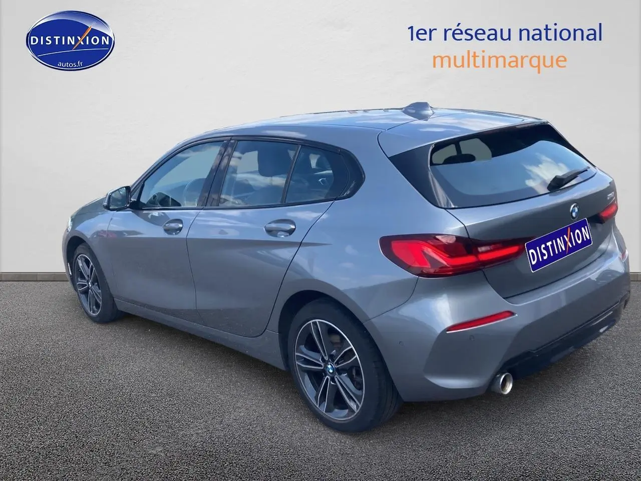 BMW Série 1 gris foncé vue 3/4 arrière côté gauche, avec jantes alliage 17 pouces et feux LED arrière.