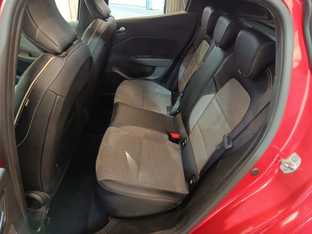 Vue intérieure arrière côté droit de la Renault Clio Techno TCe 90 rouge, sièges bicolores tissu et cuir avec surpiqûres blanches.