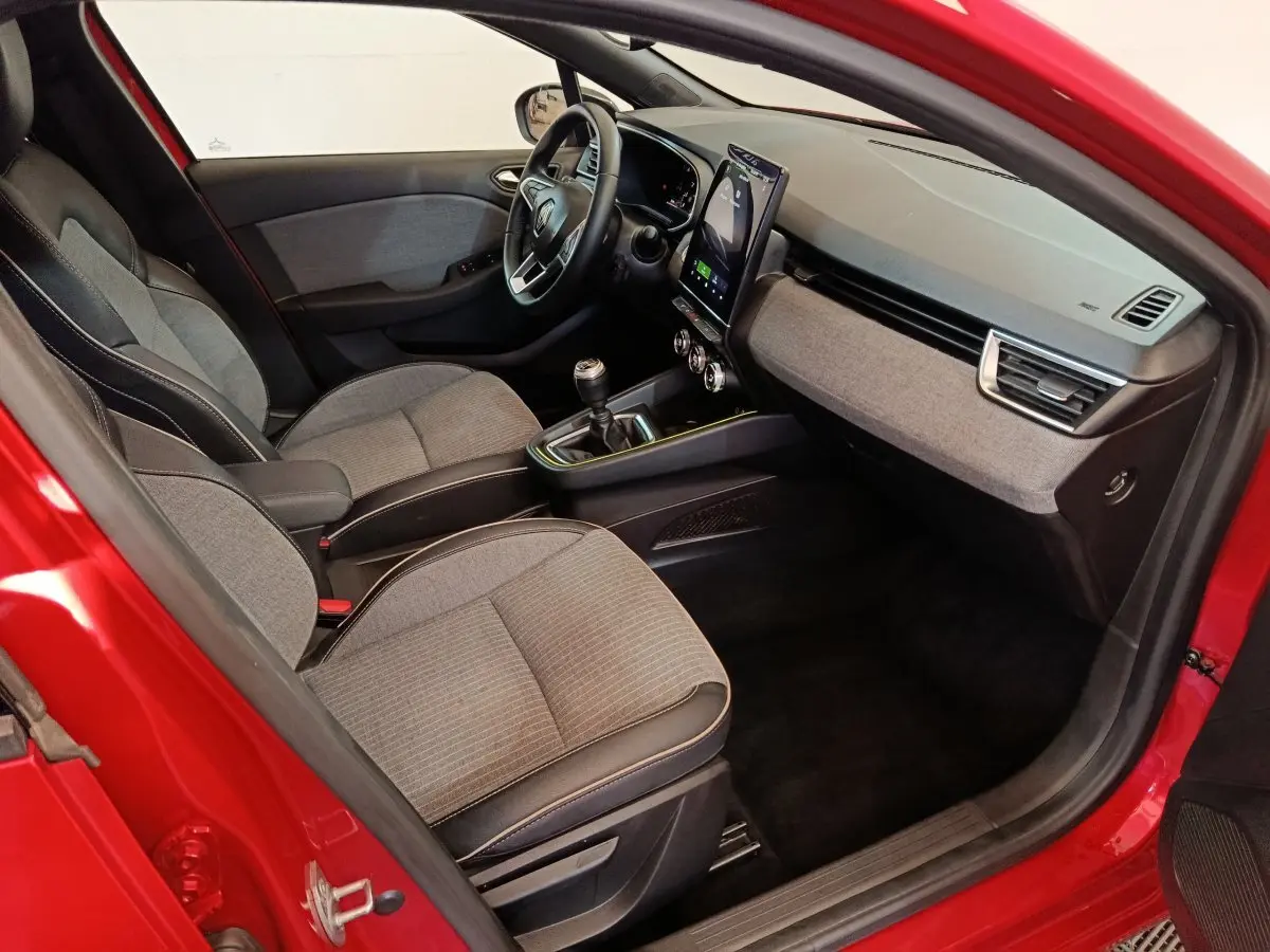 Vue intérieure côté conducteur de la Renault Clio Techno TCe 90 rouge 2024 avec tableau de bord moderne et boîte manuelle.