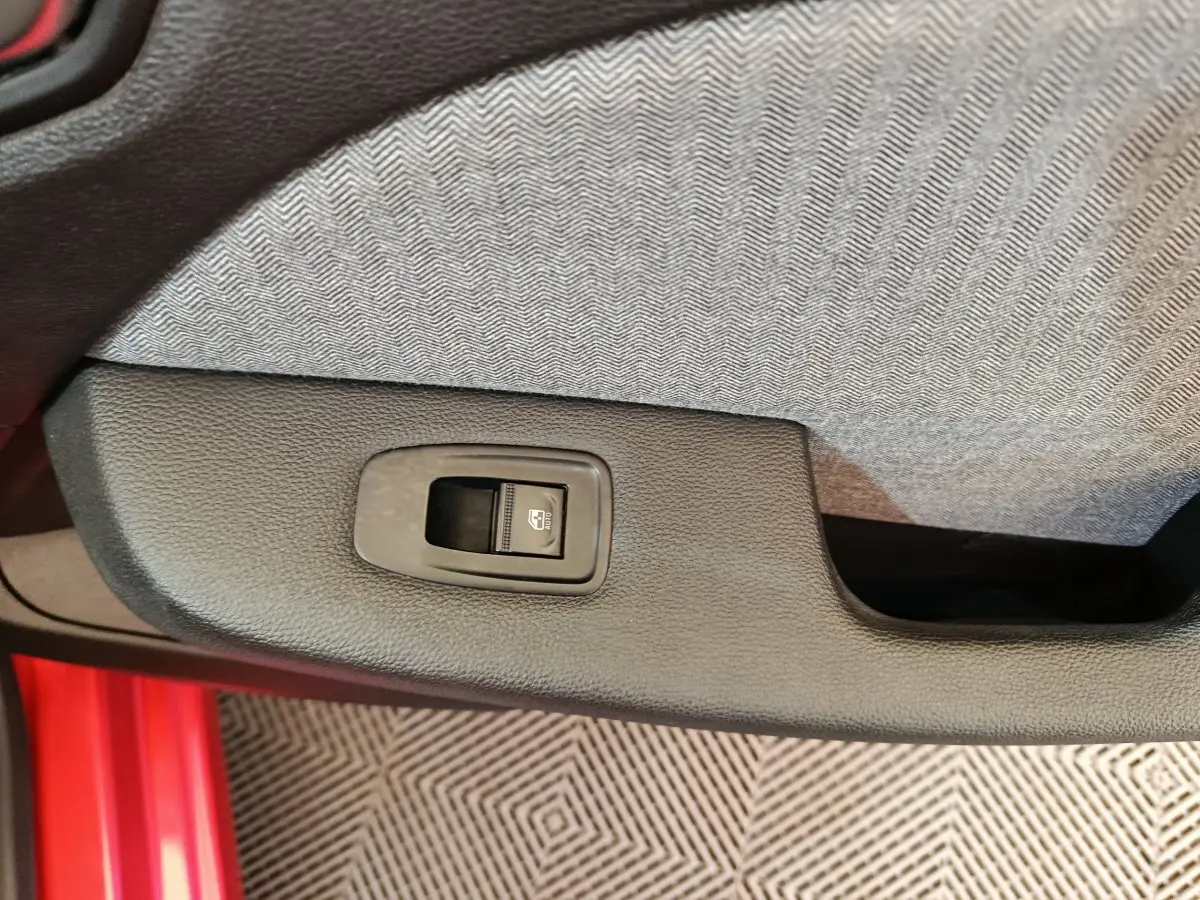 Gros plan sur le bouton de commande de la vitre arrière dans la portière côté gauche d’une Renault Clio Techno TCe 90 rouge.
