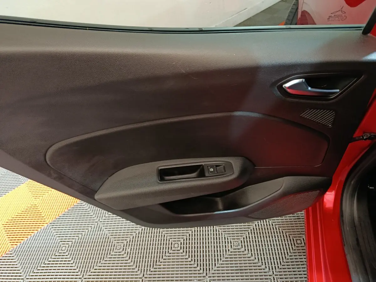 Vue intérieure de la porte avant gauche rouge de la Renault Clio 2024 avec poignée et commande de vitre noire.