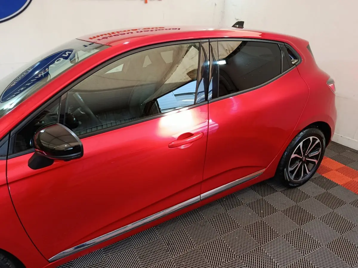 Vue de profil côté gauche d'une Renault Clio Techno TCe 90 rouge 2024 avec rétroviseur noir et jantes alliage.