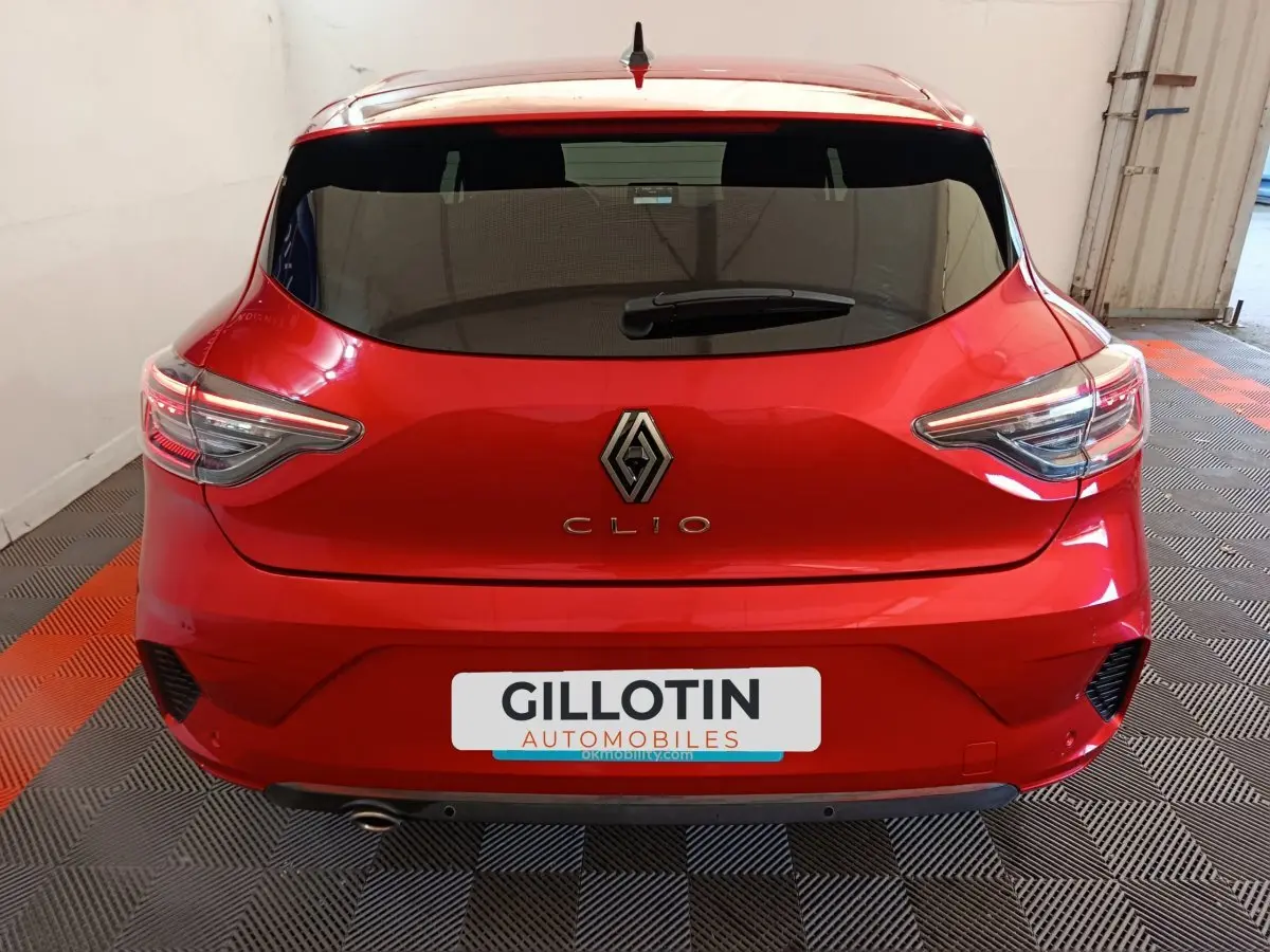 Vue arrière d'une Renault Clio rouge 2024 dans un garage, avec feux LED et logo Renault bien visibles.