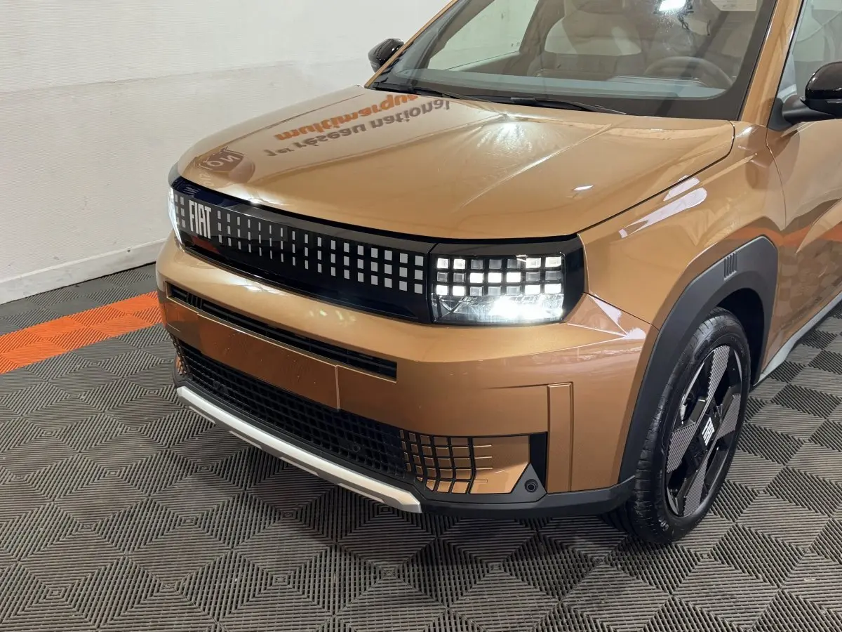 Vue 3/4 avant droite de la FIAT Grande Panda marron 2025 avec phares LED et calandre pixelisée distinctive.