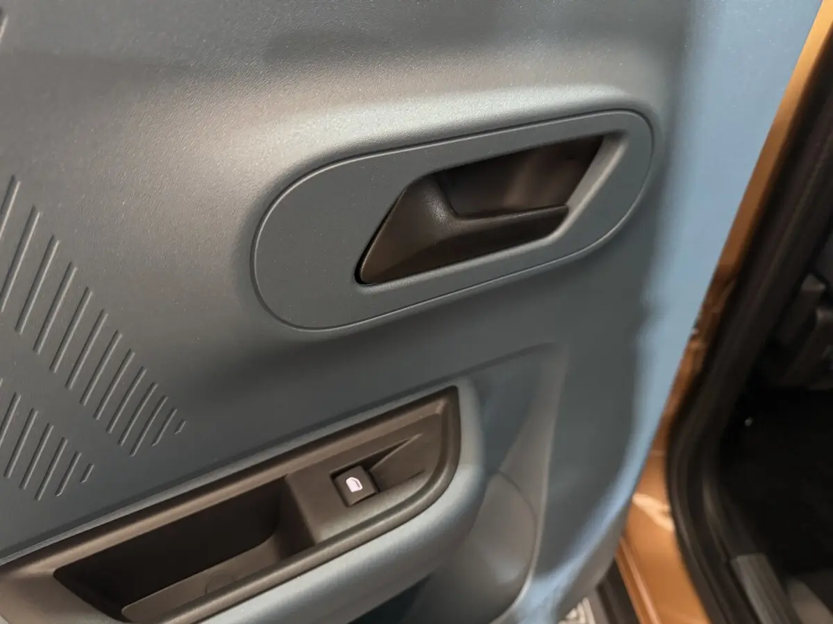 Gros plan sur la poignée intérieure et le bouton de lève-vitre côté droit d'une Fiat Grande Panda marron.