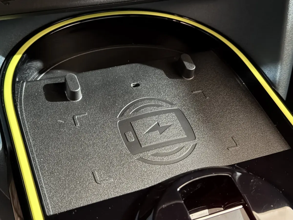 Gros plan sur la zone de recharge par induction noire avec contour jaune dans l’habitacle de la Fiat Grande Panda marron 2025.
