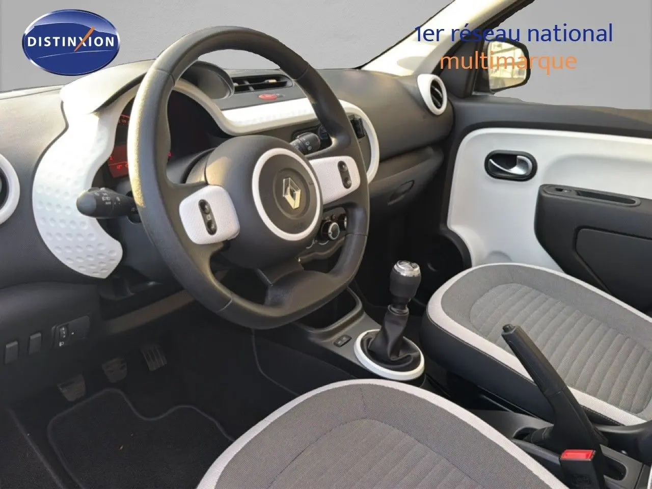 Vue intérieure côté conducteur de la Renault Twingo gris acier 2021, volant multifonction et sièges tissu gris.