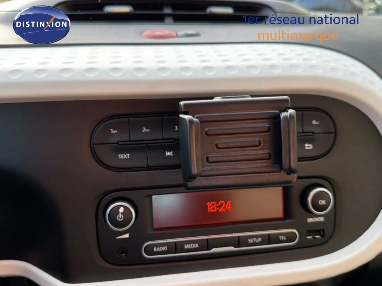 Gros plan sur la console centrale de la Renault Twingo gris acier 2021, affichant l’horloge digitale et commandes audio.