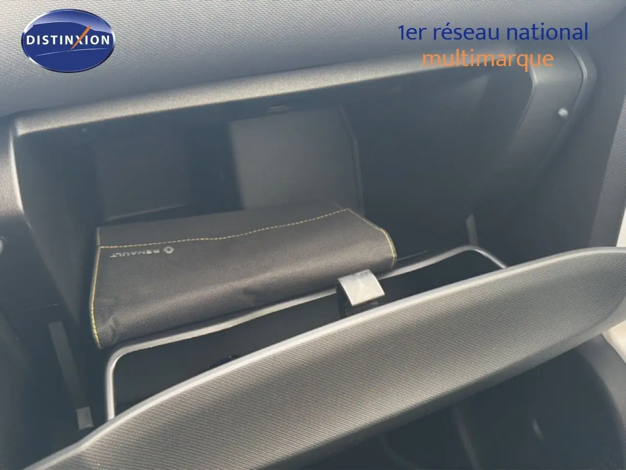 Vue intérieure du vide-poche côté passager d'une Renault Twingo gris acier, avec pochette Renault visible.