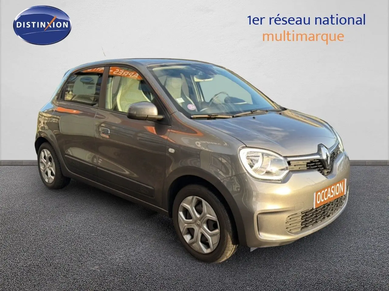Renault Twingo gris acier vue 3/4 avant droit, compacte cinq portes avec phares arrondis et jantes spécifiques.