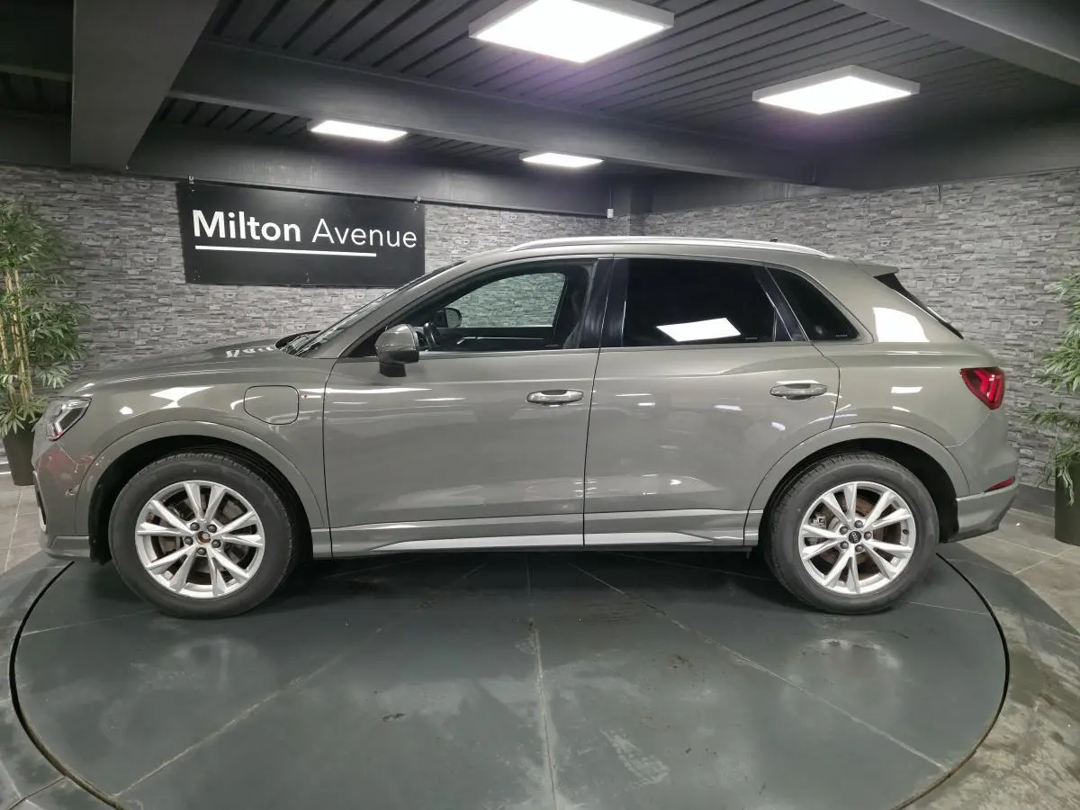 Audi Q3 gris en vue de profil côté gauche, avec jantes alliage et vitres arrière surteintées dans un showroom.