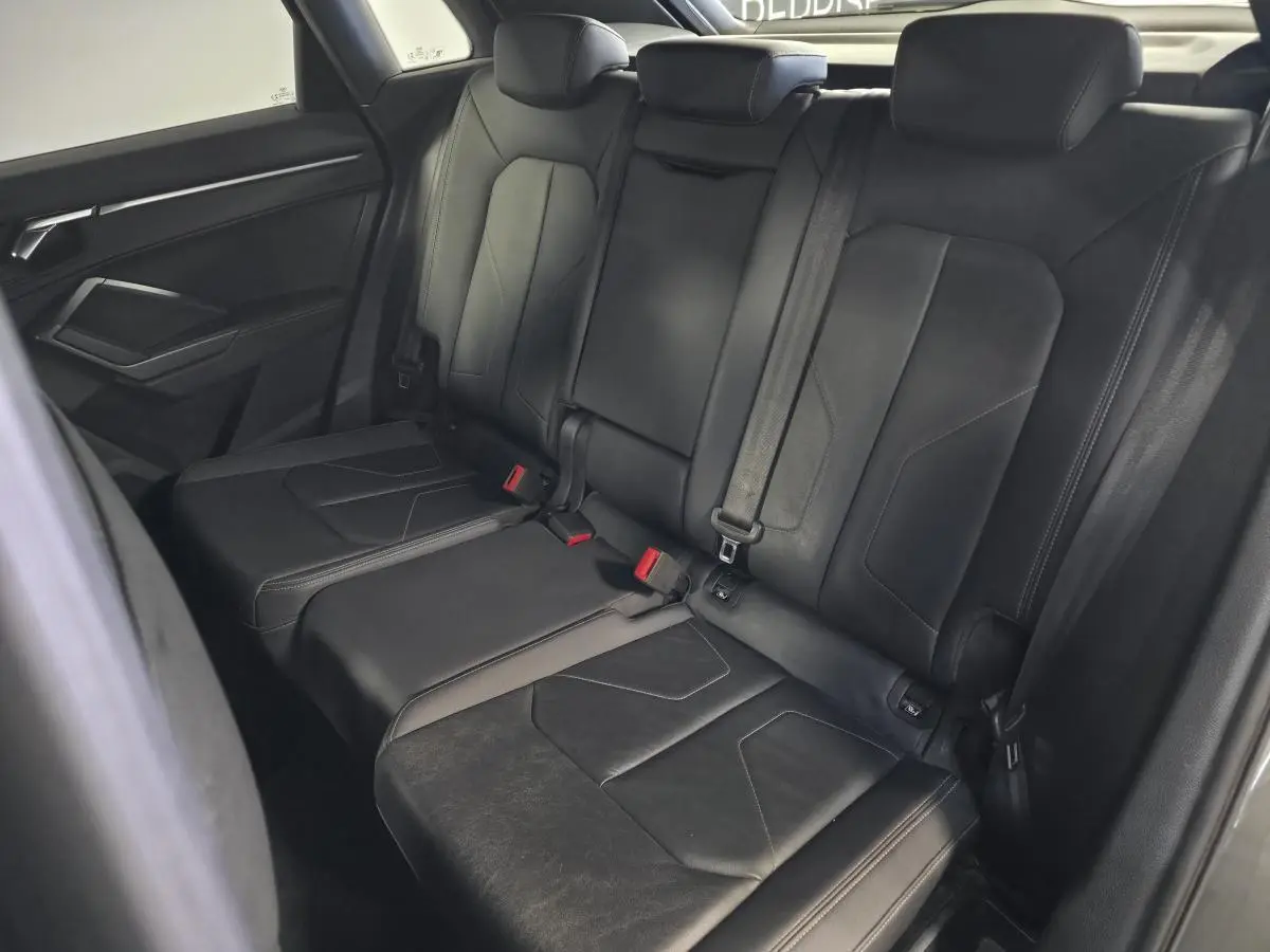 Vue intérieure montrant la banquette arrière en cuir noir de l'Audi Q3 S Line avec ceintures de sécurité et appuie-têtes.