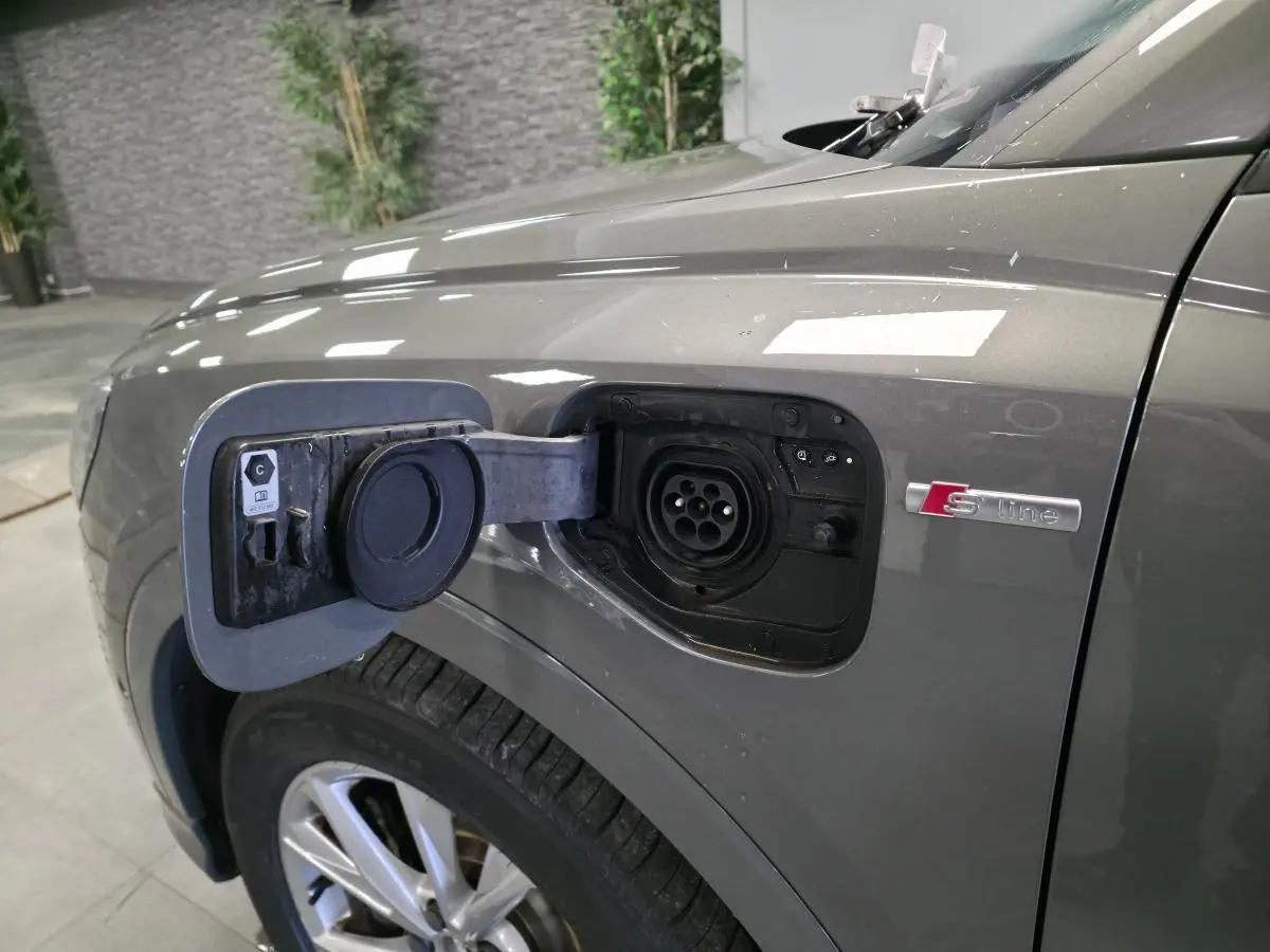Prise de recharge ouverte sur le côté gauche d’un Audi Q3 gris S line, avec jante 5 branches visible.