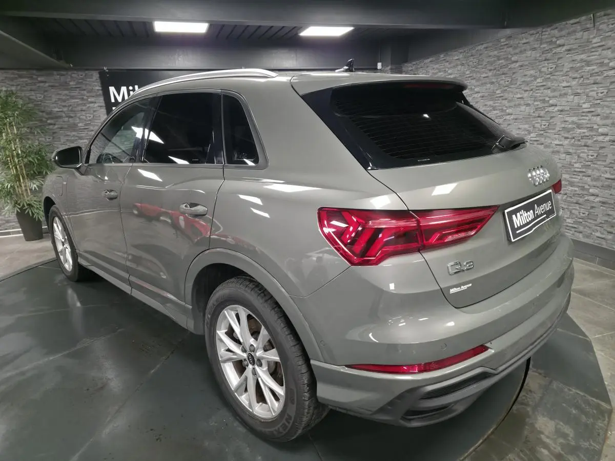 Audi Q3 gris métallisé en vue 3/4 arrière droit, avec vitres surteintées et feux arrière LED distinctifs.