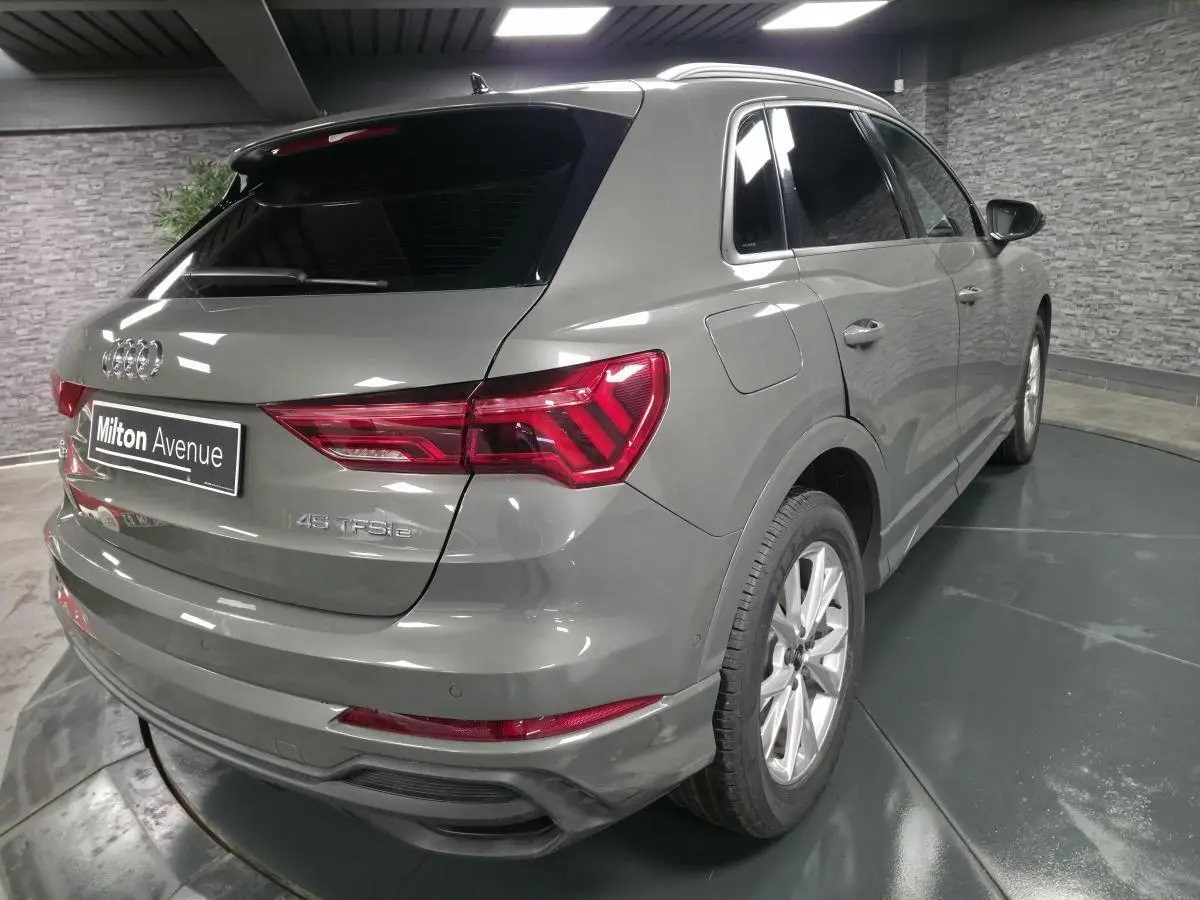 Audi Q3 gris en 3/4 arrière droit, avec vitres surteintées et feux arrière LED distinctifs.