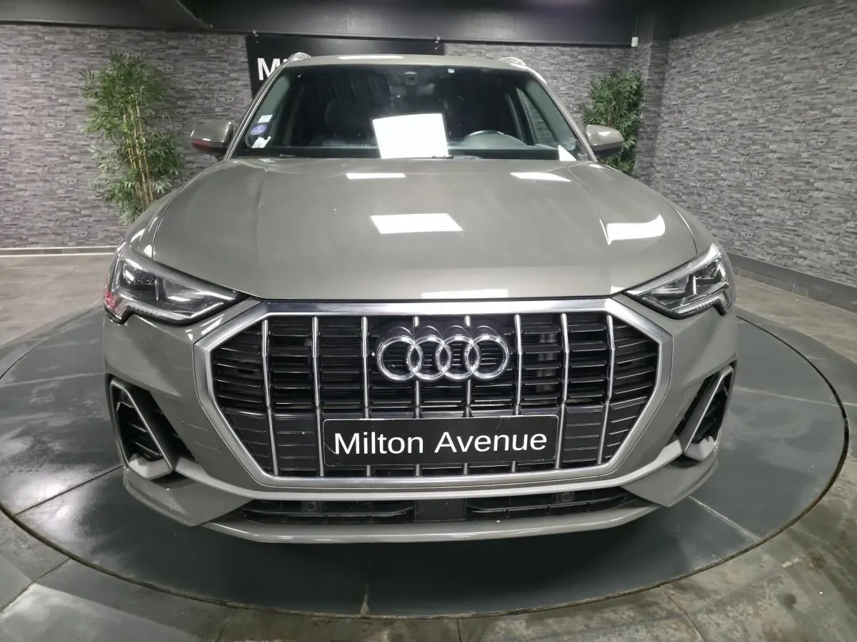 Vue avant d'un Audi Q3 gris métallisé avec calandre noire et phares Matrix LED dans un showroom.