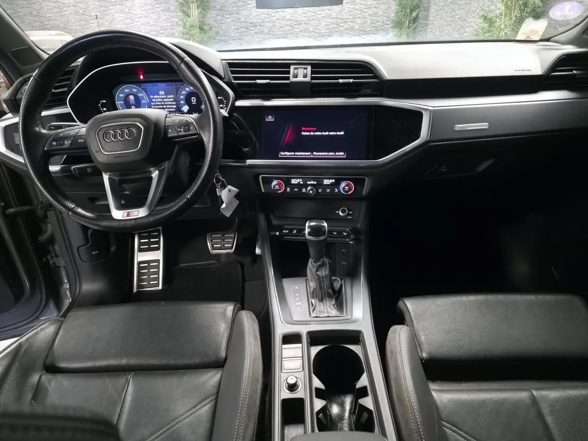 Vue intérieure avant de l'Audi Q3 gris, avec volant sport, tableau de bord numérique et console centrale moderne.