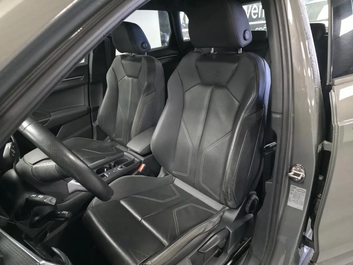 Vue intérieure côté conducteur de l'Audi Q3 gris, mettant en valeur les sièges sport en cuir noir avec surpiqûres.