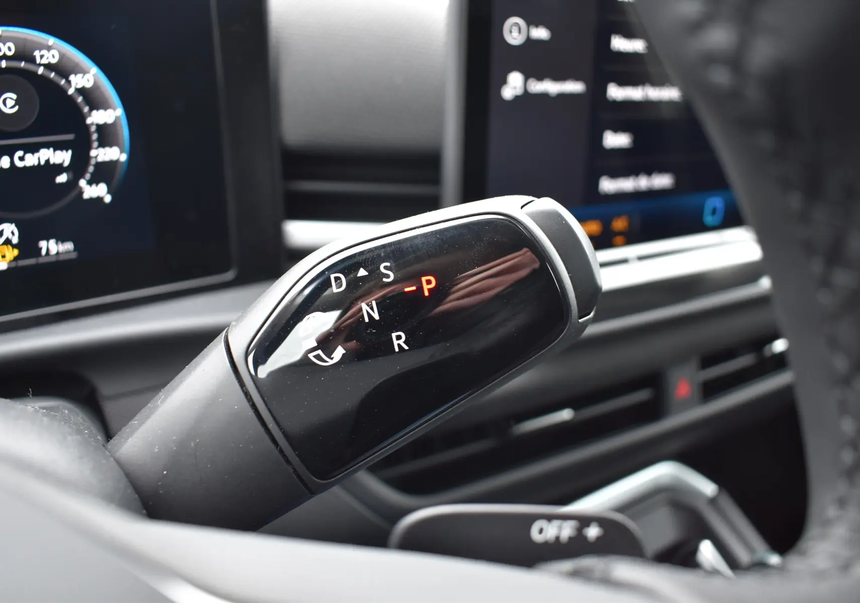 Gros plan sur le levier de vitesses automatique noir du Volkswagen T-Roc 2025, tableau de bord numérique en arrière-plan.