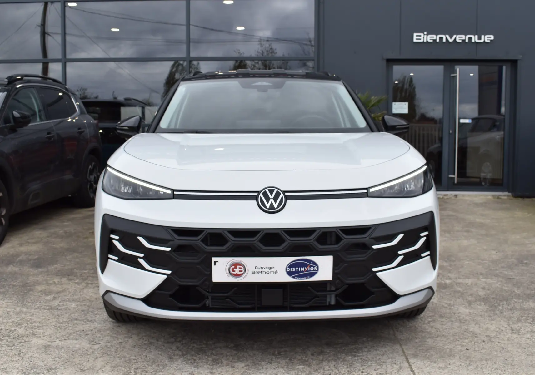 Vue frontale d'un Volkswagen T-Roc blanc 2025 avec calandre noire hexagonale et feux LED fins.