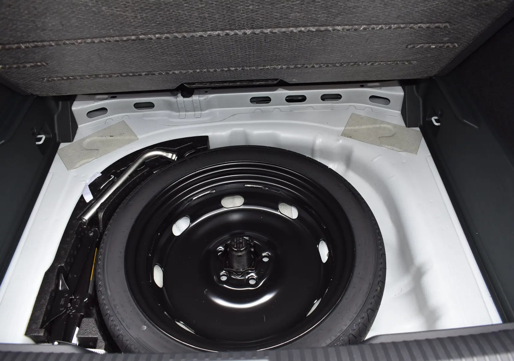 Vue du coffre avec roue de secours noire et compartiment blanc du Volkswagen T-Roc blanc 2025 hybride essence.