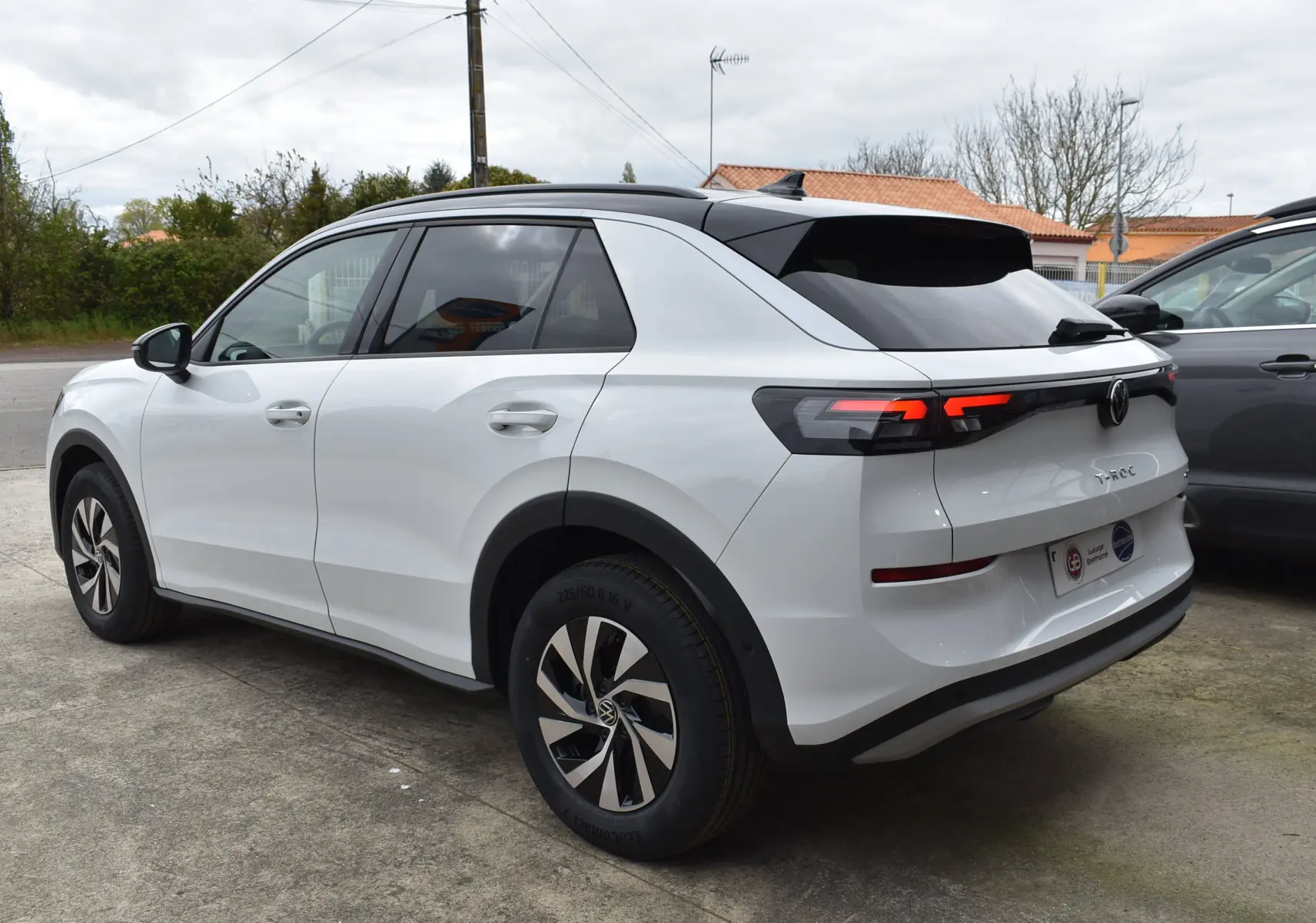 Volkswagen T-Roc blanc vue 3/4 arrière droit, toit noir, jantes alliage et feux arrière LED distinctifs.