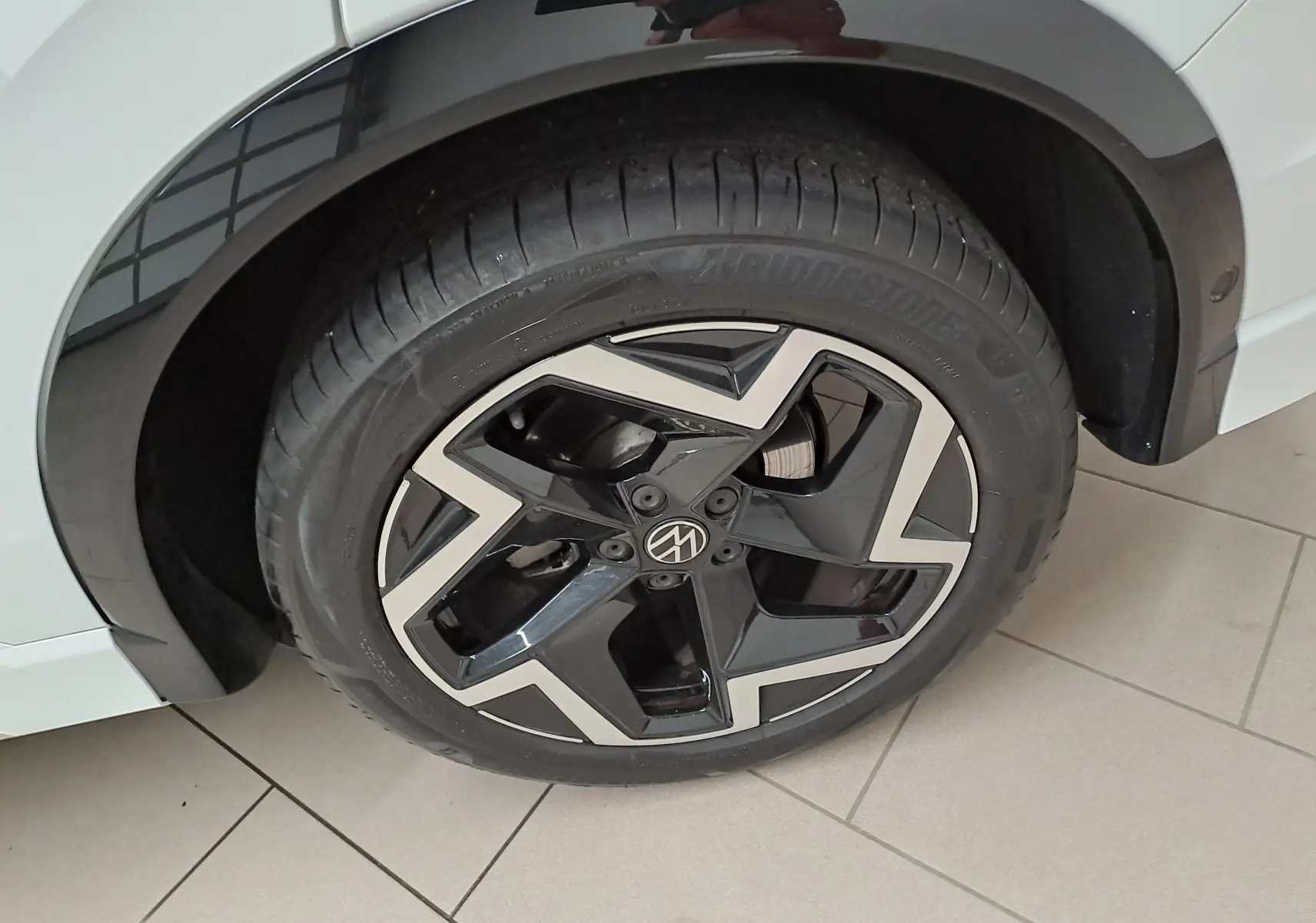 Gros plan sur la roue avant gauche du Volkswagen Tiguan blanc pur, jante alliage noire et argentée R-Line.