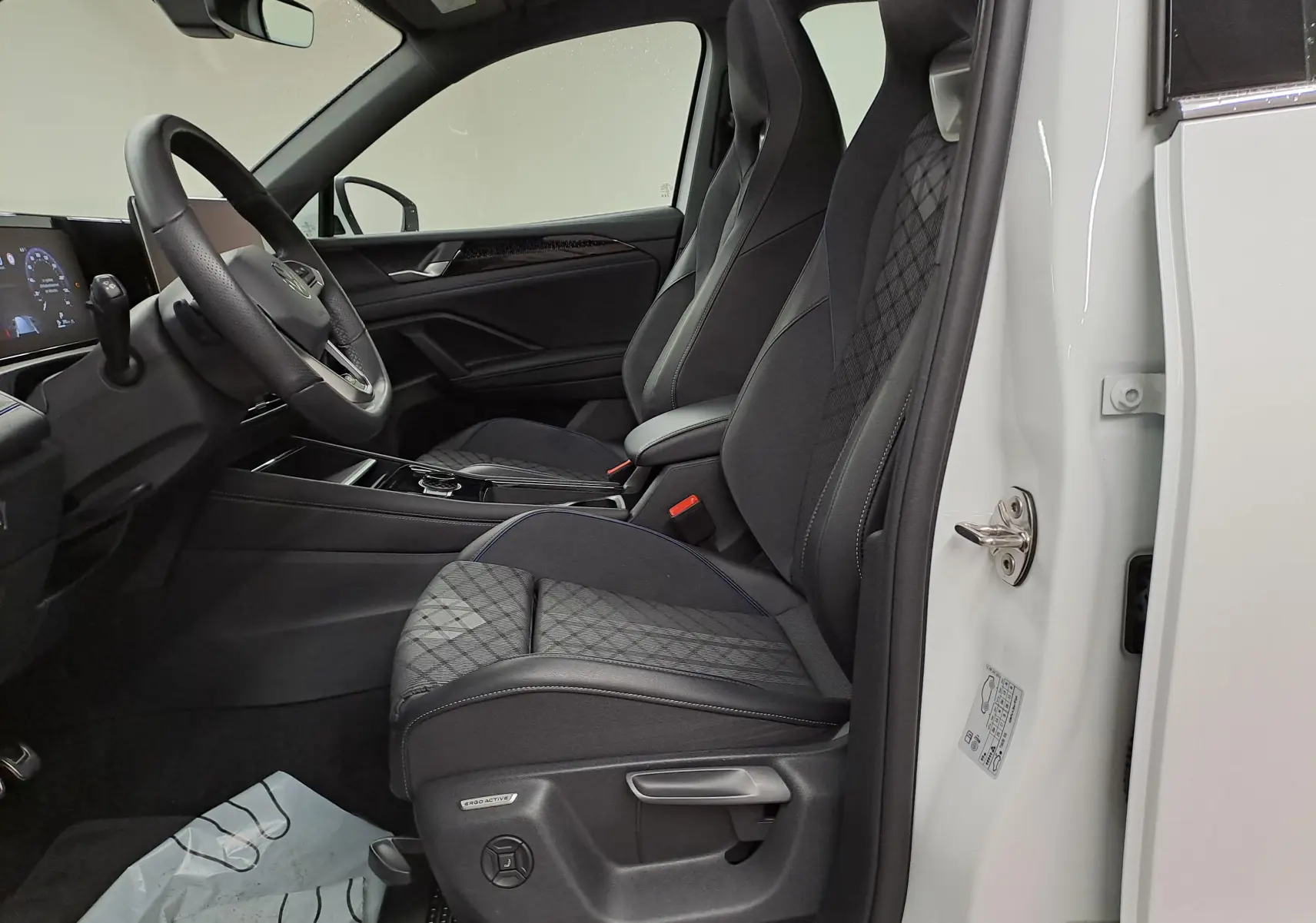 Vue intérieure côté conducteur du Volkswagen Tiguan blanc pur 2025, sièges tissu noir avec surpiqûres et console moderne.