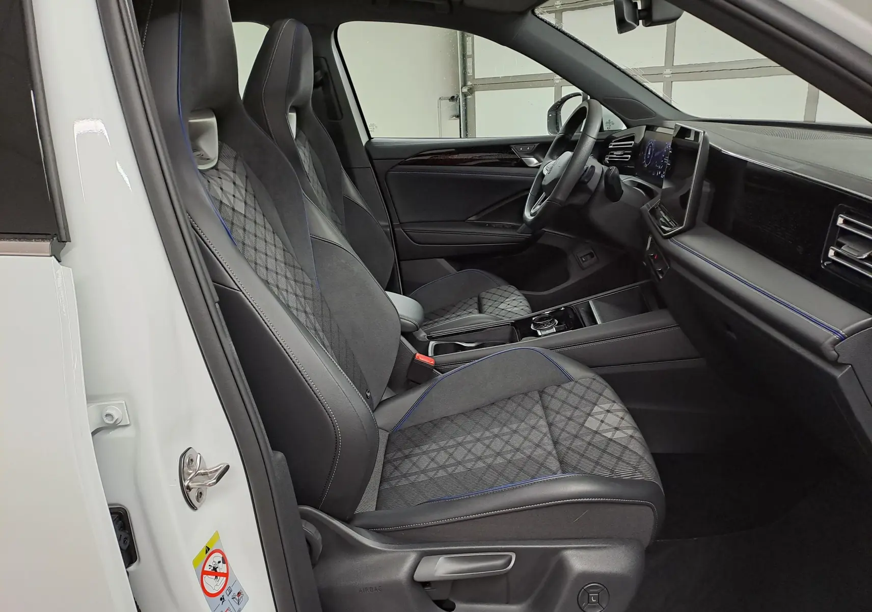 Vue intérieure côté conducteur du Volkswagen Tiguan blanc pur 2025, sièges sport R-Line avec surpiqûres bleues et tableau de bord moderne.
