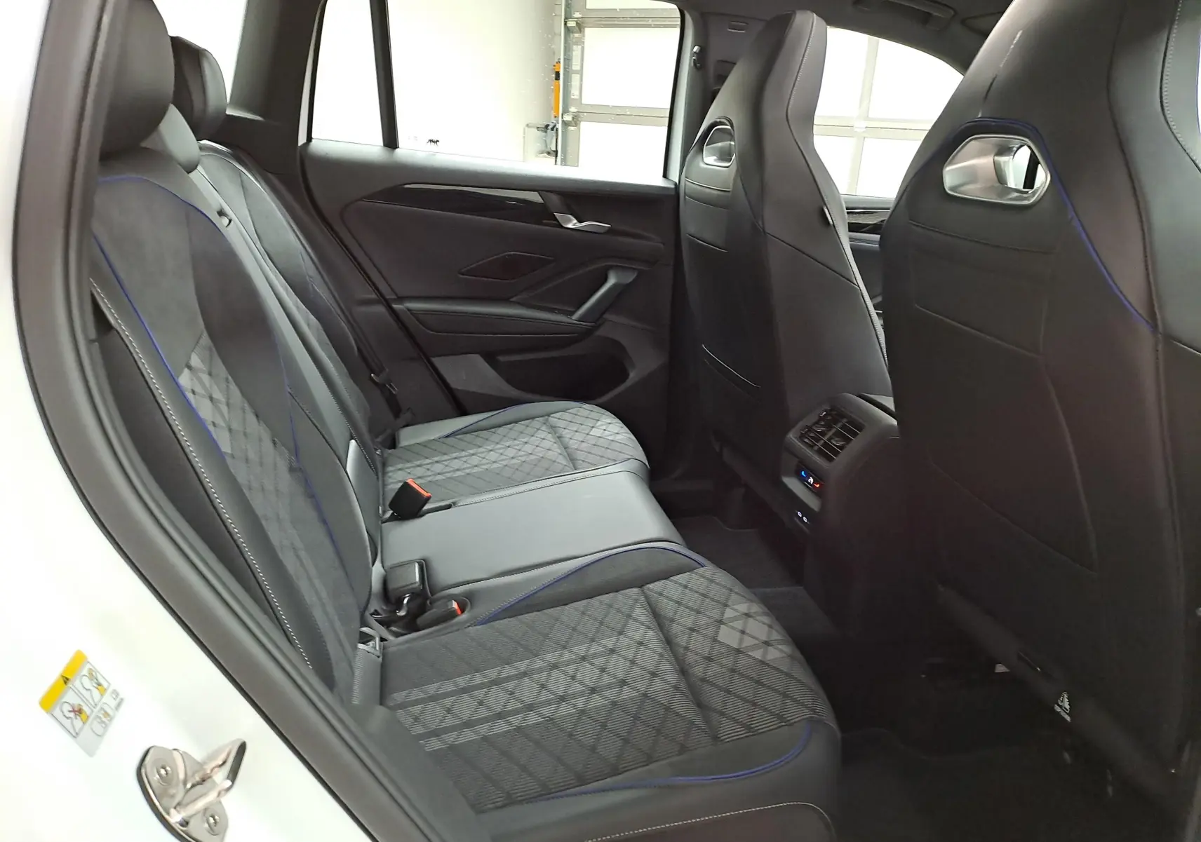 Vue intérieure arrière côté gauche du Volkswagen Tiguan 2025 blanc pur, sièges en tissu et cuir avec surpiqûres bleues.