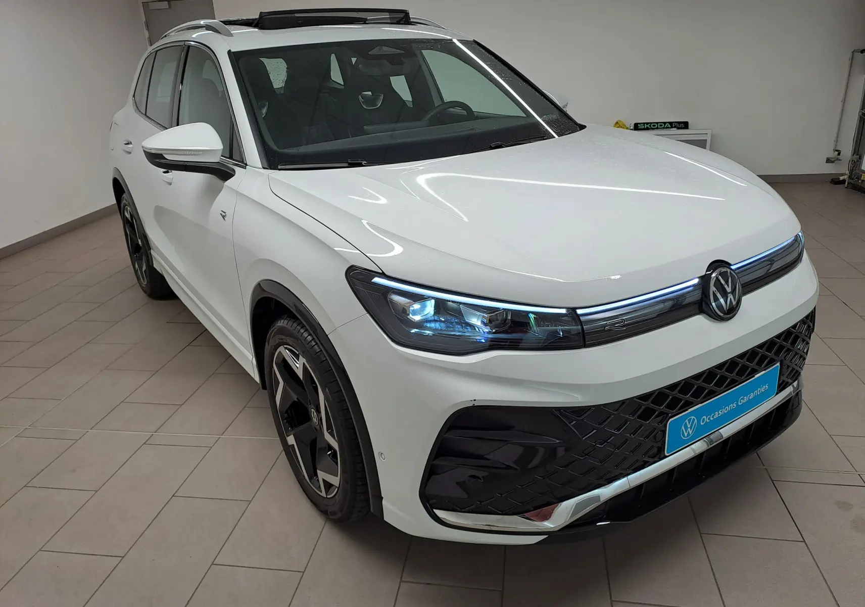 Vue 3/4 avant droite du Volkswagen Tiguan blanc pur 2025 R-Line avec phares LED et jantes noires distinctives.