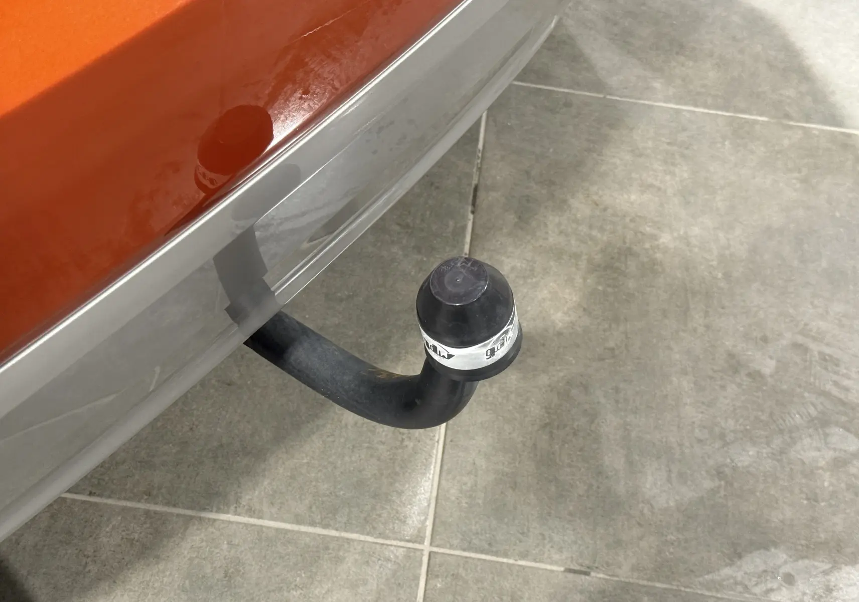 Gros plan sur l'attelage arrière noir d'un Suzuki Ignis orange 2022, vue partielle du pare-chocs gris.