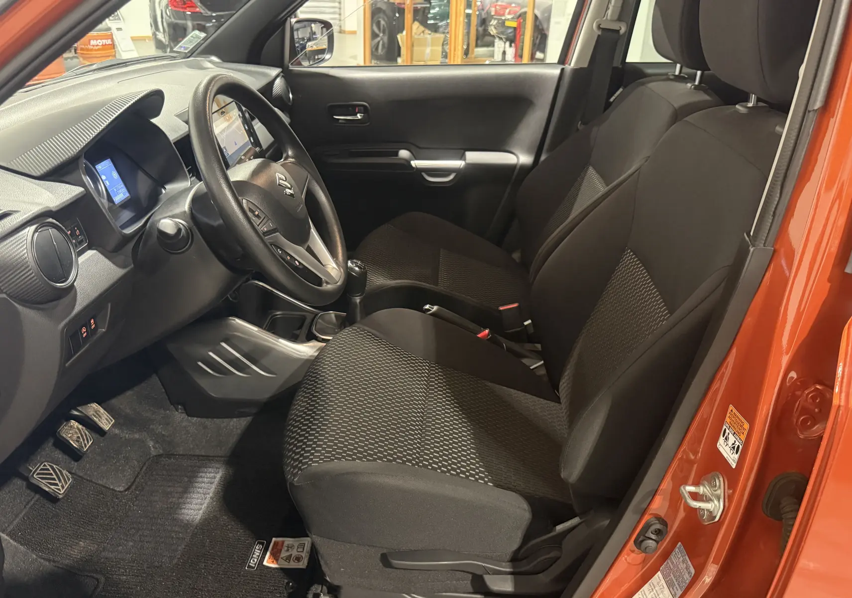 Intérieur avant droit de la Suzuki Ignis 2022 orange, montrant les sièges noirs et le volant avec boîte manuelle.