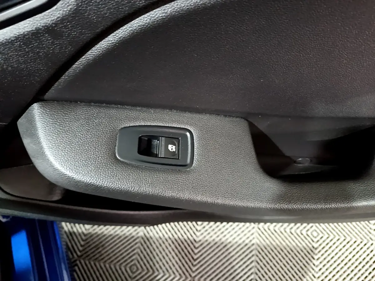 Gros plan sur le bouton de verrouillage centralisé sur la porte intérieure noire d'une Renault Clio bleu visible en bas.