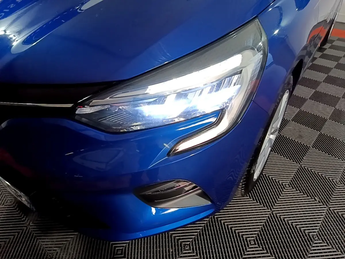 Gros plan sur l'avant droit de la Renault Clio Business bleu, mettant en valeur son phare LED allumé et la calandre.