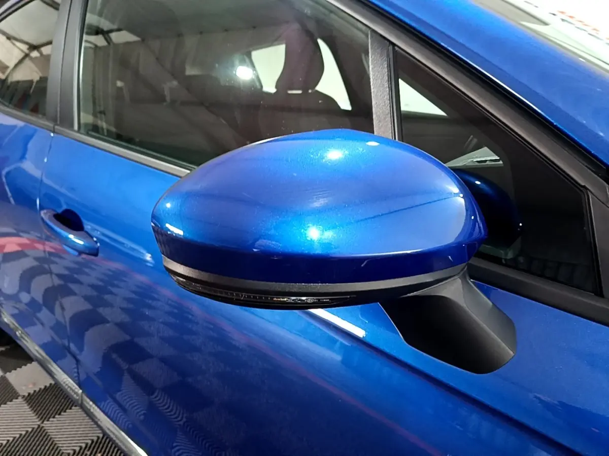 Gros plan sur le rétroviseur côté conducteur bleu métallisé d'une Renault Clio Business 2022, avec porte et vitre visibles.