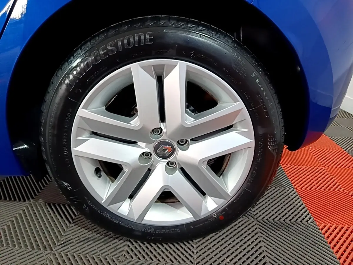 Vue rapprochée de la roue arrière droite d'une Renault Clio Business bleu vif sur sol à damier noir et rouge.