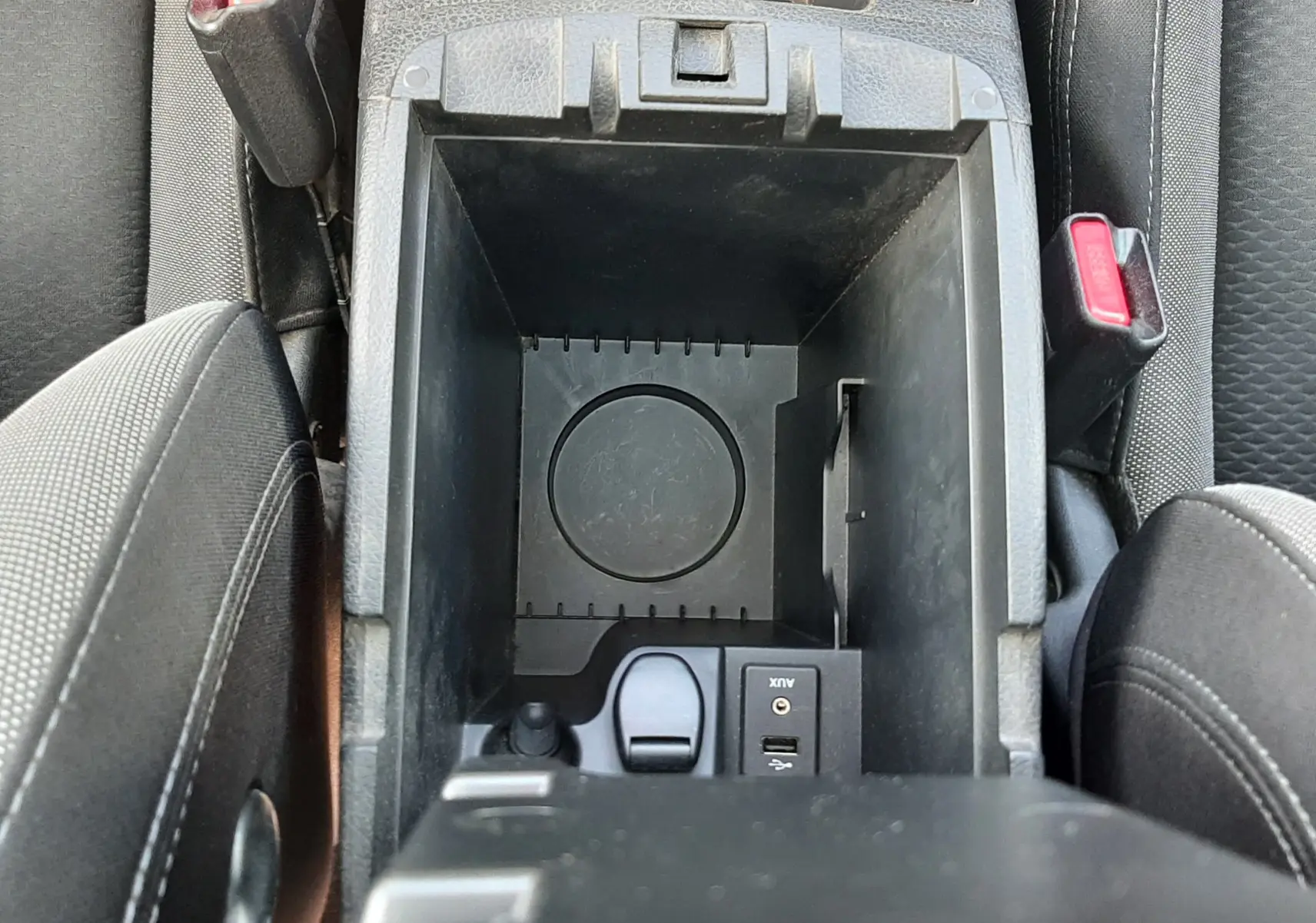 Vue plongeante sur le rangement central noir du Nissan Qashqai 2018 avec boutons de sièges chauffants et ceintures visibles.