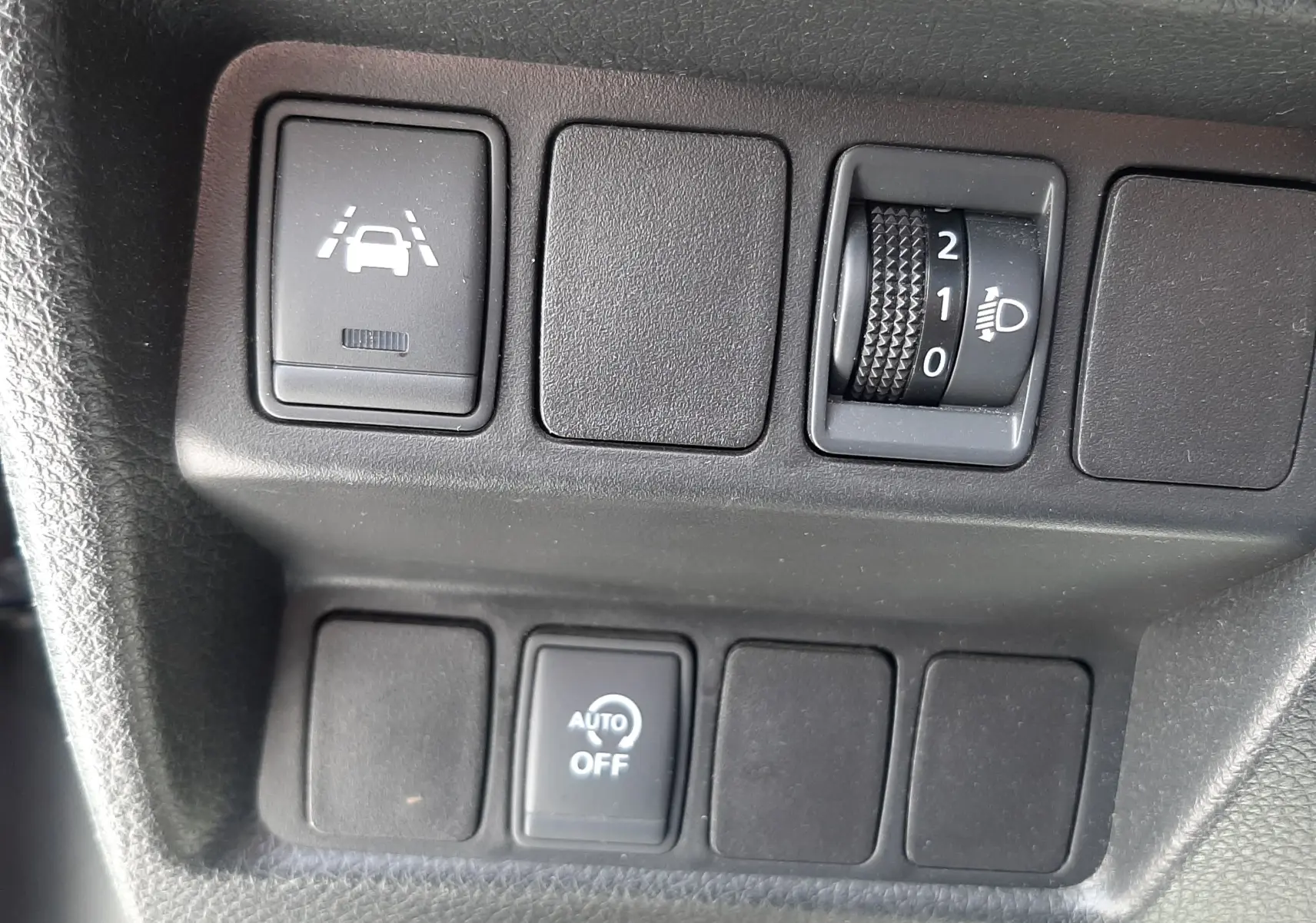 Gros plan sur les commandes intérieures noires du Nissan Qashqai 1.2 DIG-T 2018, avec réglage phares et assistance de maintien de voie.