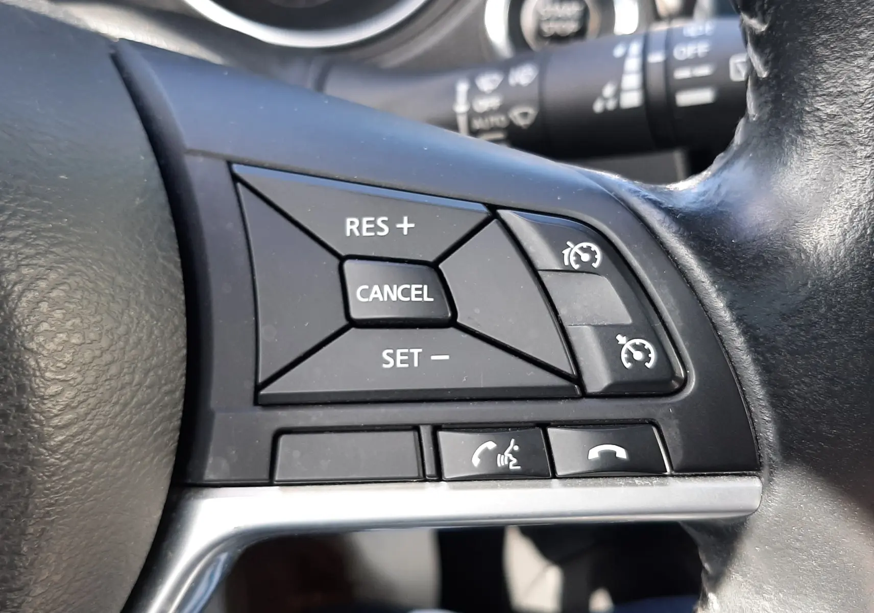 Gros plan sur les commandes de régulateur de vitesse et téléphone au volant noir du Nissan Qashqai 2018.