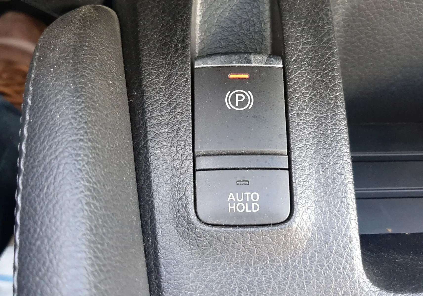 Gros plan sur les boutons de frein à main électronique et Auto Hold en plastique noir dans l'habitacle du Nissan Qashqai marron métal.