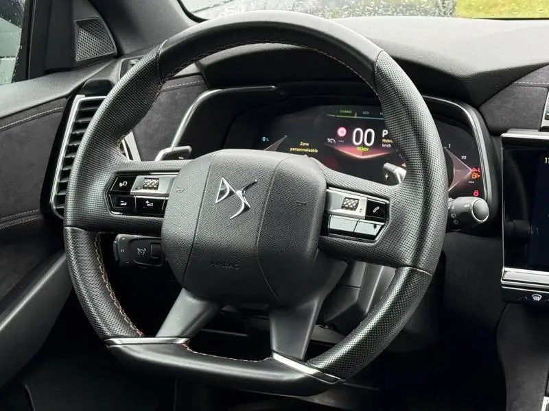 Vue rapprochée du volant cuir noir du DS7 E-TENSE 2024 avec tableau de bord numérique et commandes intégrées.
