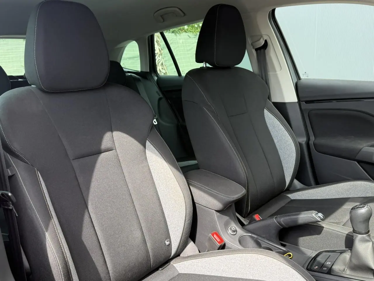 Vue intérieure des sièges avant noirs et gris d'une Skoda Scala TSI 116 Sélection avec accoudoir central et levier de vitesses manuel.