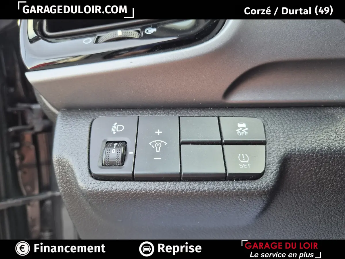Gros plan sur les commandes de réglage des phares et du contrôle de traction d’une KIA STONIC 1.0 T-GDi 2019, intérieur noir.