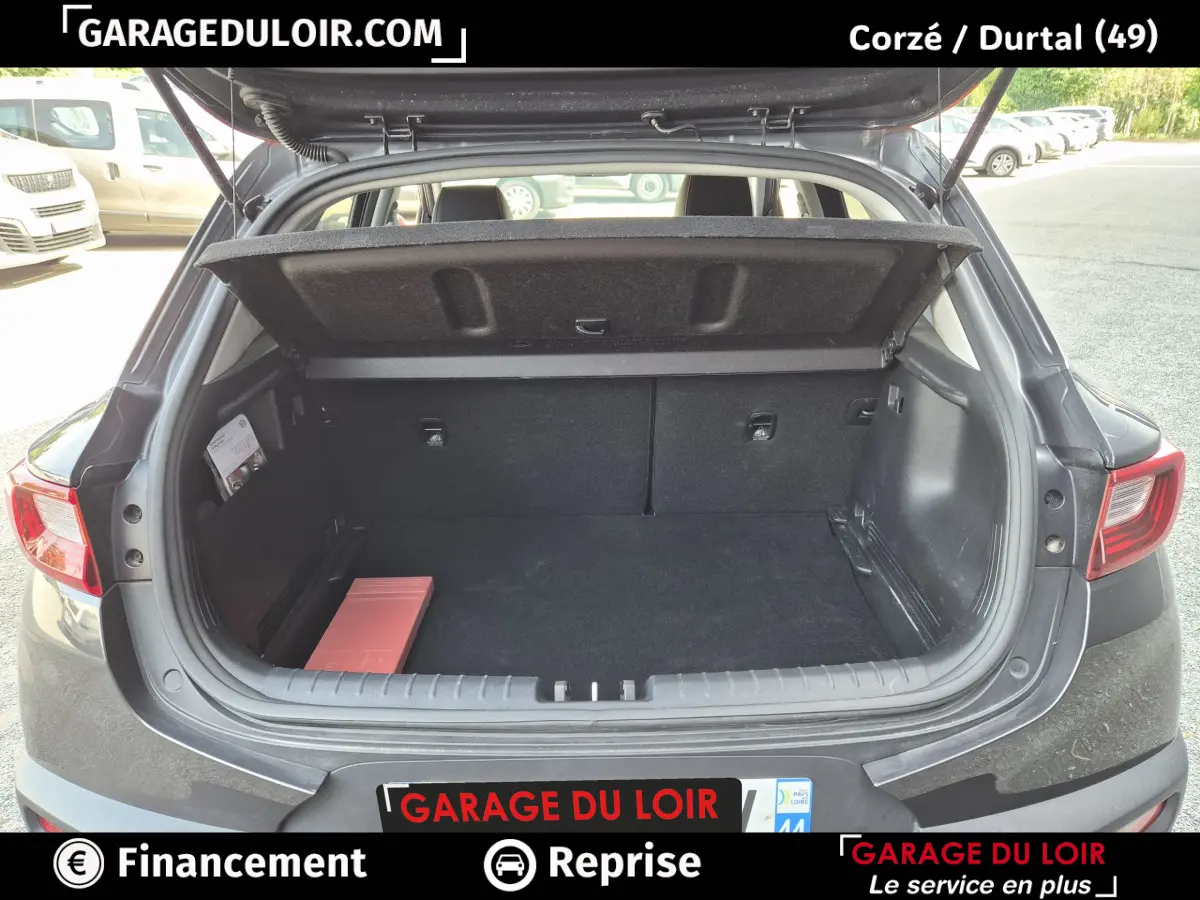 Coffre ouvert vue arrière d’une KIA STONIC 1.0 T-GDi 100 ACTIVE gris foncé avec cache-bagages relevé.