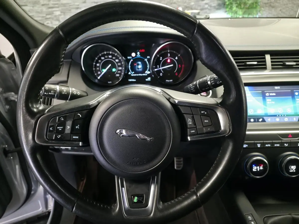 Vue centrée sur le volant cuir noir du Jaguar E-PACE gris, avec tableau de bord numérique et écran tactile visible à droite.